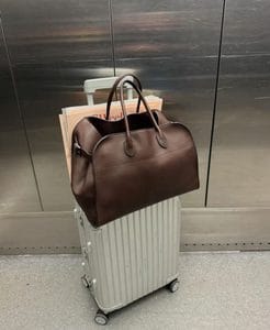Brown leather duffle bag with rolled handles sitting on top of a silver hardshell suitcase