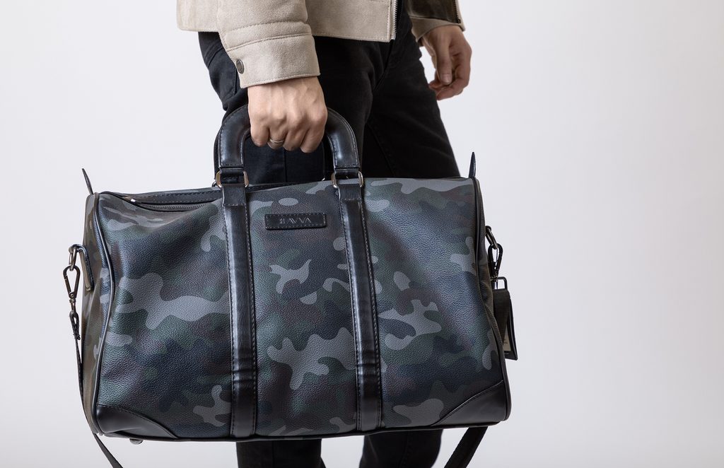 Man carrying a camouflage print leather duffel bag with black handles and shoulder strap, a practical weekender style
